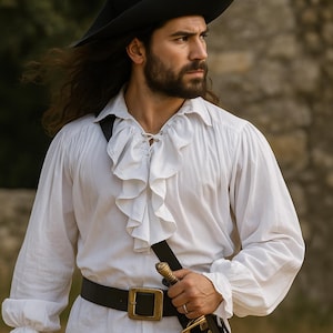 May include: A white ruffled shirt with long sleeves, a black belt with a gold buckle, and a black hat. The shirt has a lace-up neckline. A sword is attached to a black strap.