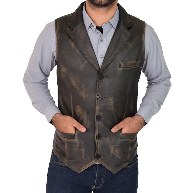 May include: A distressed brown leather vest with a notched lapel, three buttons, and two front pockets. The vest is worn over a light blue button-down shirt and dark blue jeans. The vest has a vintage, worn look.