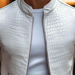 Pode incluir: Casaco de couro branco com textura de pele de r&eacute;ptil, gola alta e z&iacute;per completo. Usado sobre uma camiseta branca, o casaco apresenta um design moderno e elegante.