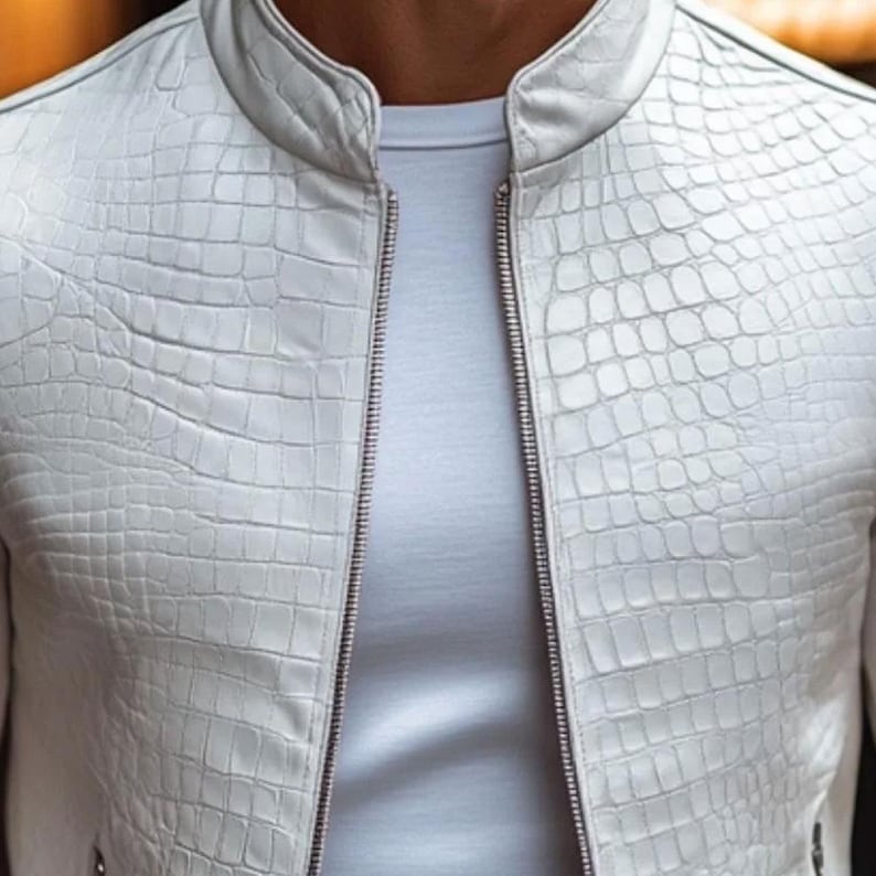 Pode incluir: Casaco de couro branco com textura de pele de r&eacute;ptil, gola alta e z&iacute;per completo. Usado sobre uma camiseta branca, o casaco apresenta um design moderno e elegante.