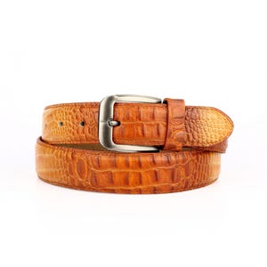 May include: A brown leather belt with a silver buckle. The belt has a textured, crocodile-like pattern. The buckle is rectangular with rounded edges. The belt is approximately 1.5 inches wide.