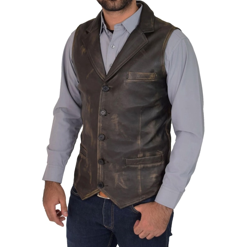 May include: A brown leather vest with a distressed finish, featuring a notched lapel, three buttons, and two front pockets. The vest is worn over a gray button-down shirt and blue jeans. The vest appears to be made of genuine leather.