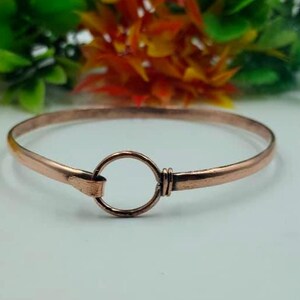 Puede incluir: Una pulsera de color cobre con un cierre circular. La pulsera tiene un diseño sencillo y elegante. El fondo presenta flores coloridas. El diámetro de la pulsera es de aproximadamente 6 cm.