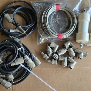 May include: An assortment of electronic components, including coiled black cables with connectors, a bundle of gray cables, and various metal connectors. Two white cylindrical components are also present.