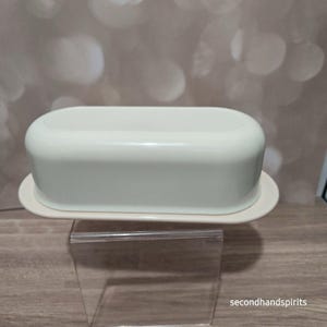 May include: A smooth, off-white butter dish with a rounded, oblong lid and a matching base. The container features a clean, minimalist design with a glossy finish, providing a simple and functional storage solution for a standard stick of butter.