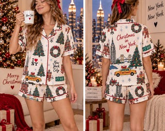 May include: A two-piece pajama set featuring a short-sleeve button-down shirt and matching shorts in an off-white fabric. The print displays New York City landmarks, Christmas trees, wreaths, yellow taxis, and text reading Christmas in New York.