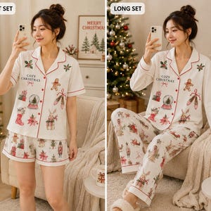 May include: A two-piece pajama set in white with red piping, featuring a button-down top and matching bottoms. The fabric is printed with Christmas motifs including gingerbread men, snow globes, and stockings, with the text Cozy Christmas.