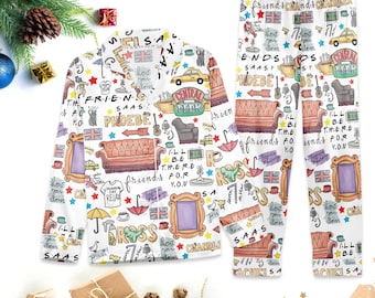 May include: White pajama set featuring a colorful pattern with text and illustrations from the TV show "Friends." The set includes a long-sleeved top and matching pants. The design incorporates iconic elements like the Central Perk logo and the orange couch.