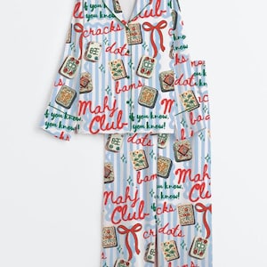 Peut inclure: Un ensemble pyjama compos&eacute; d'une chemise &agrave; manches longues boutonn&eacute;e et d'un pantalon assorti, avec un motif &agrave; rayures verticales bleu clair et blanc. Le tissu est imprim&eacute; de tuiles de mah-jong, de n&oelig;uds rouges et du texte Mahj Club et if you know, you know.