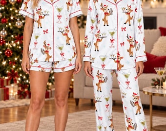 May include: A white pajama set featuring a repeating pattern of reindeer holding martini glasses and cocktail shakers, accented with red piping. The set includes a short-sleeved button-down top with shorts, and a long-sleeved button-down top with long pants.