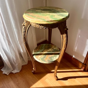 Può includere: Un tavolino vintage con piano rotondo in marmo verde e oro e ripiano inferiore abbinato. Il tavolo ha gambe dorate ornate e una cornice decorativa. Il tavolo è alto circa 61 cm.