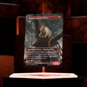 May include: A trading card featuring "Ragavan, Nimble Pilferer," a Monkey Pirate. The card has a detailed illustration of a monkey on a ship. The card's text includes "Legendary Creature - Monkey Pirate" and other game details.