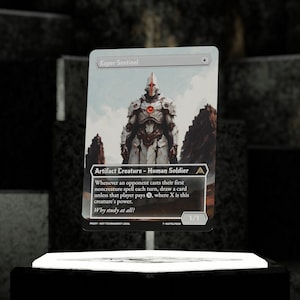 May include: A trading card featuring the "Esper Sentinel." The card depicts a futuristic armored figure in white and silver, set against a landscape. The card text includes game rules and the phrase "Why study at all?"