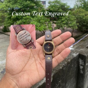 May include: A brown leather compass watch with a brass bezel and a dark face. The watch strap is brown leather. The image also shows a close-up of the watch's engraved plate with the text "Curiosity and Ambition over Apathy and Fear - SF". The text "Custom Text Engraved" is at the top.