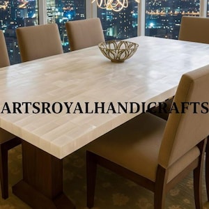 Puede incluir: Una mesa de comedor rectangular con una superficie clara estampada y una base marrón oscuro. Seis sillas tapizadas beige rodean la mesa. Un cuenco decorativo está sobre la mesa. El texto "ARTSROYALHANDICRAFTS" está impreso en la mesa.