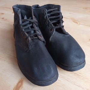 Puede incluir: Un par de botines de cuero negro con punta redondeada, cierre frontal de cordones con ojales oscuros y cordones negros. Las botas tienen un acabado mate texturizado en la superficie de cuero y una suela de perfil bajo.
