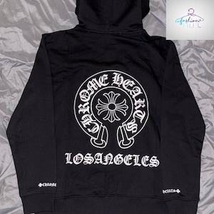 May include: Black hoodie with a white graphic on the back that says "CHROME HEARTS LOSANGELES". The hoodie has a drawstring hood and a small logo on the left sleeve.