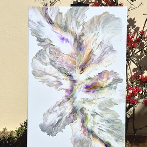 May include: Abstract acrylic painting on canvas. The artwork features a central, organic form with flowing lines and a mix of colors, including white, gray, purple, and gold. The painting is displayed outdoors, leaning against a wall.