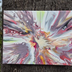 May include: Abstract acrylic pour painting on canvas. The artwork features a burst of colors, including red, white, yellow, and gray, creating a dynamic and textured effect. The painting is displayed against a natural tree trunk background.