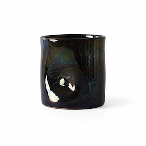 Peut inclure: Une tasse cylindrique en céramique avec une glaçure sombre et brillante présentant des reflets irisés bleus et verts. La surface a une finition noire profonde et réfléchissante avec des variations de couleurs subtiles et une forme courbe.