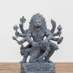 May include: A gray sculpture of a deity with a lion's head and multiple arms, holding various objects. The figure is depicted in a dynamic pose, with a creature beneath its feet. The sculpture is on a decorative base.