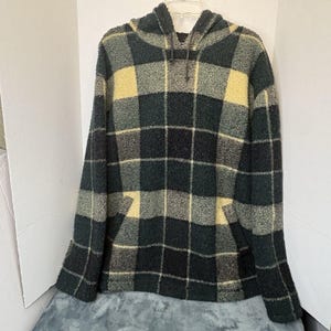 May include: A hooded sweatshirt in a plaid pattern. The colors are dark green, light green, and yellow. The sweatshirt has a kangaroo pocket and a drawstring hood. The fabric appears to be a soft, textured material.