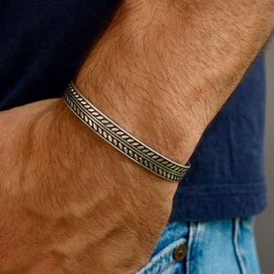 May include: Silver cuff bracelet with a detailed leaf pattern. The bracelet is worn on a wrist, showcasing the intricate design. The jewelry is a stylish accessory.