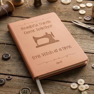 May include: A peach-colored notebook with a ribbon bookmark, featuring an embossed vintage sewing machine graphic and the text "Beautiful Things Come Together one stitch at a time" along with the name "Janet" printed on the front cover.