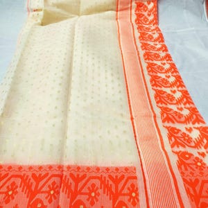 May include: Ivory-colored fabric with a delicate dotted pattern and vibrant orange borders. The borders feature intricate floral and geometric designs. The fabric is folded, showcasing the detailed patterns and textures of the material.