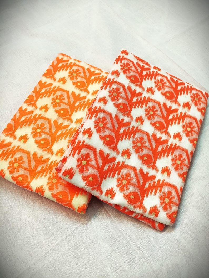 May include: Two folded fabrics with a floral pattern in orange and white. One fabric has an orange background, the other has a white background. The floral design includes stylized flowers and geometric shapes.