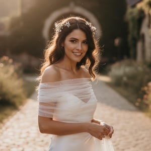 Puede incluir: Un vestido de novia blanco con hombros descubiertos que presenta un envoltorio de tul transparente adornado con peque&ntilde;as perlas blancas en el pecho y los hombros, junto a un delicado accesorio para el cabello de flores blancas.