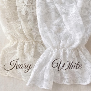 May include: Close-up of two lace fabric samples, one ivory and one white. The delicate lace is gathered at the bottom, creating a ruffled effect. The word "Ivory" is written in a cursive font on the left, and "White" on the right.
