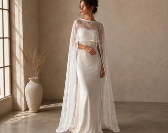 May include: A white wedding dress with a fitted bodice and a flowing skirt. The dress is paired with a delicate, lacy cape that drapes over the shoulders. The cape adds a touch of elegance and romance to the bridal ensemble.