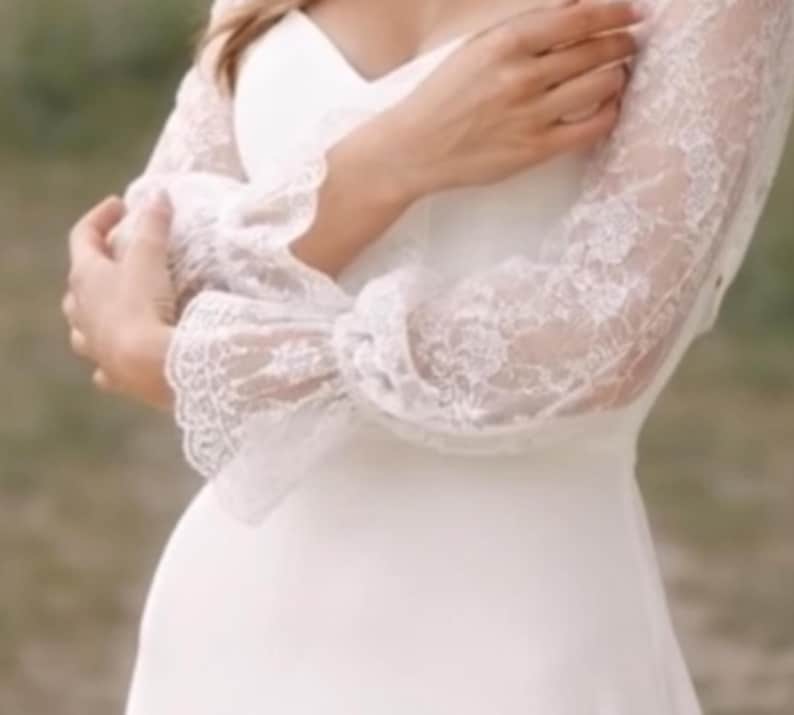 May include: A white wedding dress with long sleeves. The sleeves are made of delicate lace, and the dress has a simple, elegant design. The dress is a classic choice for a bride.