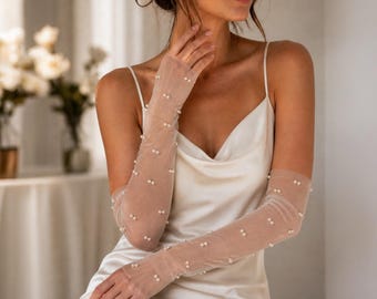 May include: Elegant, sheer ivory gloves adorned with scattered pearl embellishments. The gloves extend to the upper arm, adding a touch of sophistication. The model is wearing a satin ivory slip dress. Perfect for bridal or formal wear.