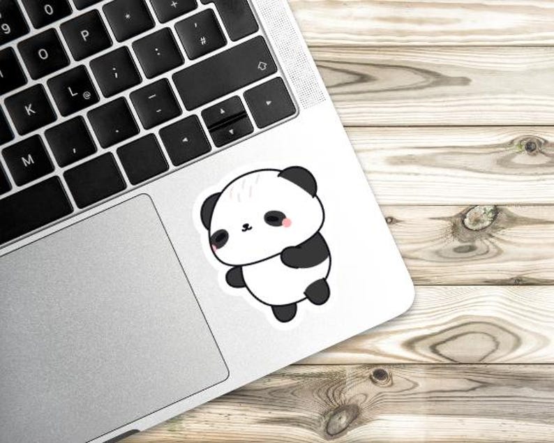 K&ouml;nnte beinhalten: Ein wei&szlig;er Aufkleber mit einem Cartoon-Panda-B&auml;ren mit schwarzen Ohren, Armen und F&uuml;&szlig;en. Der Panda hat ein kleines rosa Rouge auf den Wangen und befindet sich auf einem Laptop. Der Hintergrund ist eine Holzoberfl&auml;che.