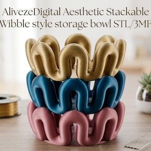 May include: A stack of three storage bowls with a wavy, wibble-style rim. The top bowl is metallic gold, the middle is dark blue, and the bottom is dusty pink. The text reads: AlivezeDigital Aesthetic Stackable Wibble style storage bowl STL/3MF.