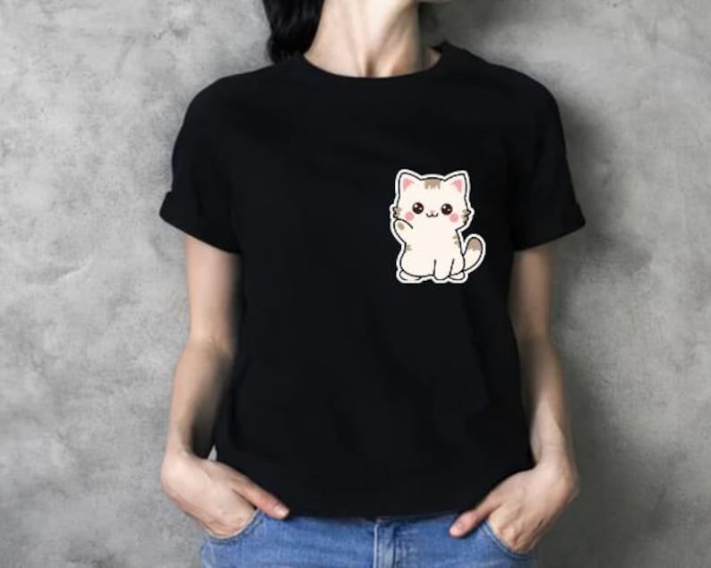 K&ouml;nnte beinhalten: Schwarzes T-Shirt mit einem niedlichen Cartoon-Katzen-Motiv auf der Vorderseite. Die Katze ist wei&szlig; mit braunen Akzenten und winkt. Das Shirt hat kurze &Auml;rmel und einen Rundhalsausschnitt.