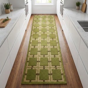 Op de afbeelding: Een rechthoekig groen en beige patroonkleed. Het kleed heeft een herhalend geometrisch ontwerp van groene vierkanten en beige verbindingslijnen. Het kleed ligt op een houten vloer in een keuken.