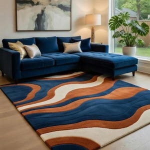May include: A modern living room featuring a navy blue sectional sofa with gold and silver accent pillows. A patterned rug with blue, orange, and white wave designs sits on the hardwood floor. A large abstract painting hangs above the sofa.