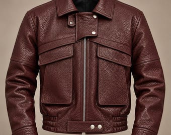 May include: A deep burgundy leather jacket with a textured grain finish, featuring a central silver zipper, a fold-down collar, two large front flap pockets, and silver snap button closures on the collar, cuffs, and waist hem.