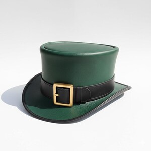 May include: A green top hat with a black band and a gold-colored buckle. The hat has a wide brim and a cylindrical crown. The hat is made of a smooth material and is likely leather or a leather-like material.