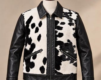 May include: A jacket featuring a black and white cow-print pattern on the front panels, contrasted with solid black leather sleeves, a black collar, and a central zipper closure. The garment includes two slanted zippered pockets on the front.