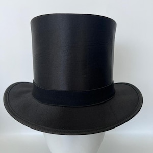 Puede incluir: Un sombrero de copa negro, un tocado formal cl&aacute;sico. Presenta una corona alta y cil&iacute;ndrica y un ala plana, con una banda negra alrededor de la base de la corona. El sombrero est&aacute; hecho de un material liso y brillante.