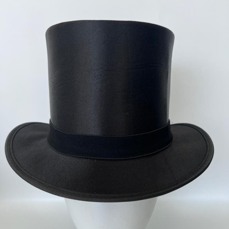 Puede incluir: Un sombrero de copa negro, un tocado formal cl&aacute;sico. Presenta una corona alta y cil&iacute;ndrica y un ala plana, con una banda negra alrededor de la base de la corona. El sombrero est&aacute; hecho de un material liso y brillante.