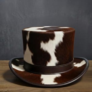 May include: A top hat with a brown and white cowhide pattern. The hat features a dark brown leather band and brim. The hat is a classic style, suitable for costumes or formal wear.