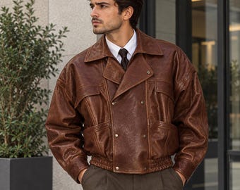 May include: A brown leather jacket with a double-breasted front, wide lapels, and a ribbed elastic waistband. The jacket features two chest pockets with flaps and metal snap buttons, worn over a white collared shirt and a dark necktie.