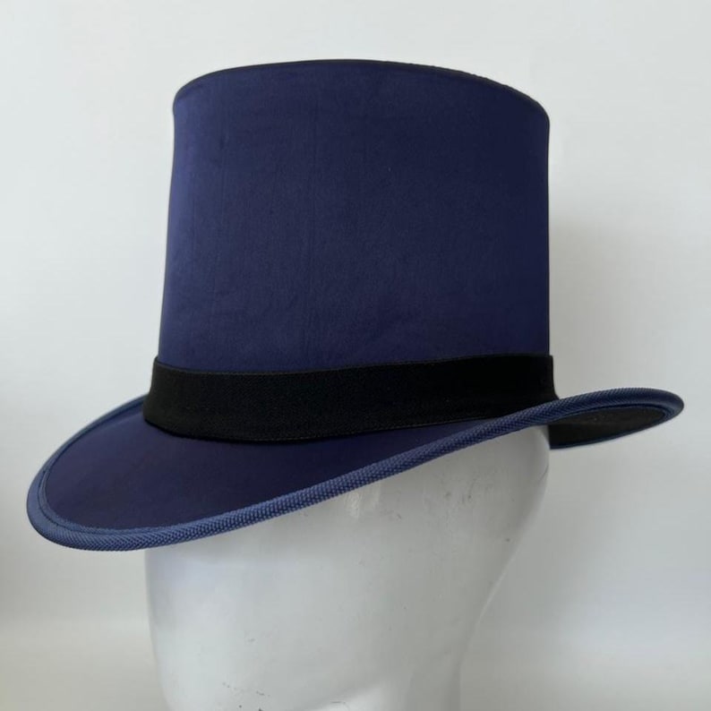 Puede incluir: Un sombrero de copa azul marino con una banda negra. El sombrero tiene una copa alta y cil&iacute;ndrica y un ala ancha y plana. El sombrero se exhibe en una cabeza de maniqu&iacute; blanca.