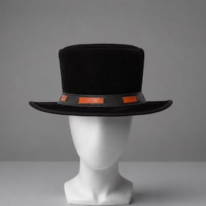 May include: A black top hat with a flat crown and a wide brim. The hat features a black leather band around the base, accented with rectangular orange leather inserts spaced evenly around the circumference of the crown.