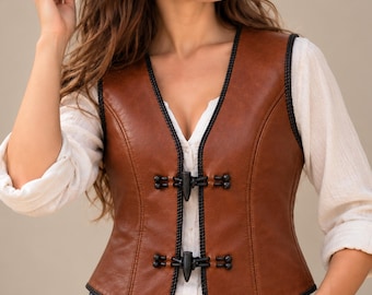 May include: A brown leather vest featuring black braided trim along the edges and two black toggle closures down the front. The vest is worn over a white long-sleeved shirt and is paired with a brown leather belt with a gold buckle.